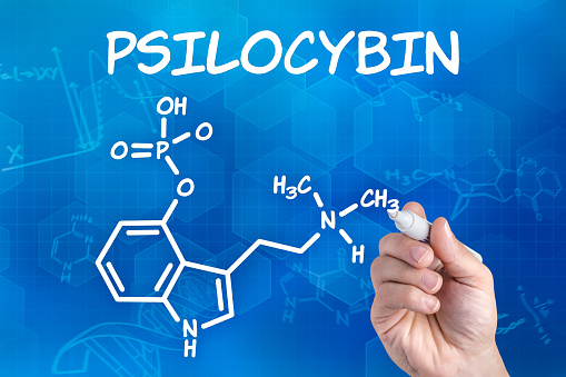 hand with pen drawing the chemical formula of psilocybin